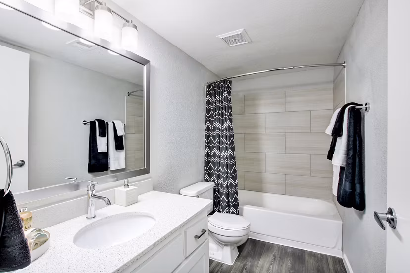Modern bathroom featuring a sleek sink, mirror, toilet, and bathtub with shower curtain in luxury apartment