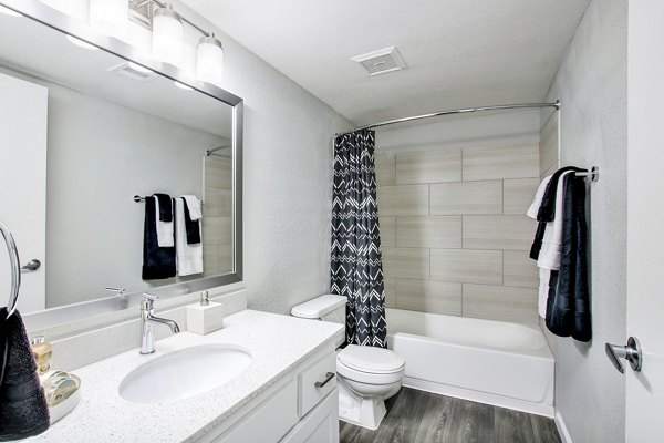 Modern bathroom featuring a sleek sink, mirror, toilet, and bathtub with shower curtain in luxury apartment