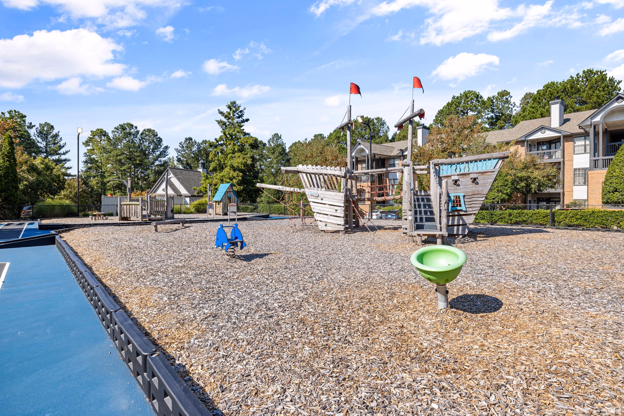 Children's playground at View at Lake Lynn Apartments with slides and climbing structures nestled in lush greenery