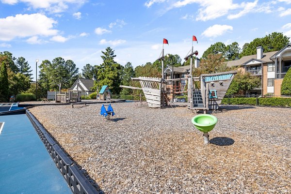 Children's playground at View at Lake Lynn Apartments with slides and climbing structures nestled in lush greenery
