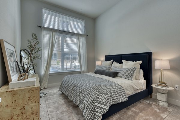 Elegant bedroom with modern decor at Encore Grayson Apartments, featuring plush bedding and ample natural light in luxury setting