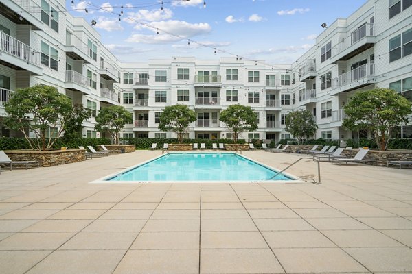 Relaxing outdoor pool area at 75 Tresser Apartments, featuring lounge chairs and lush landscaping
