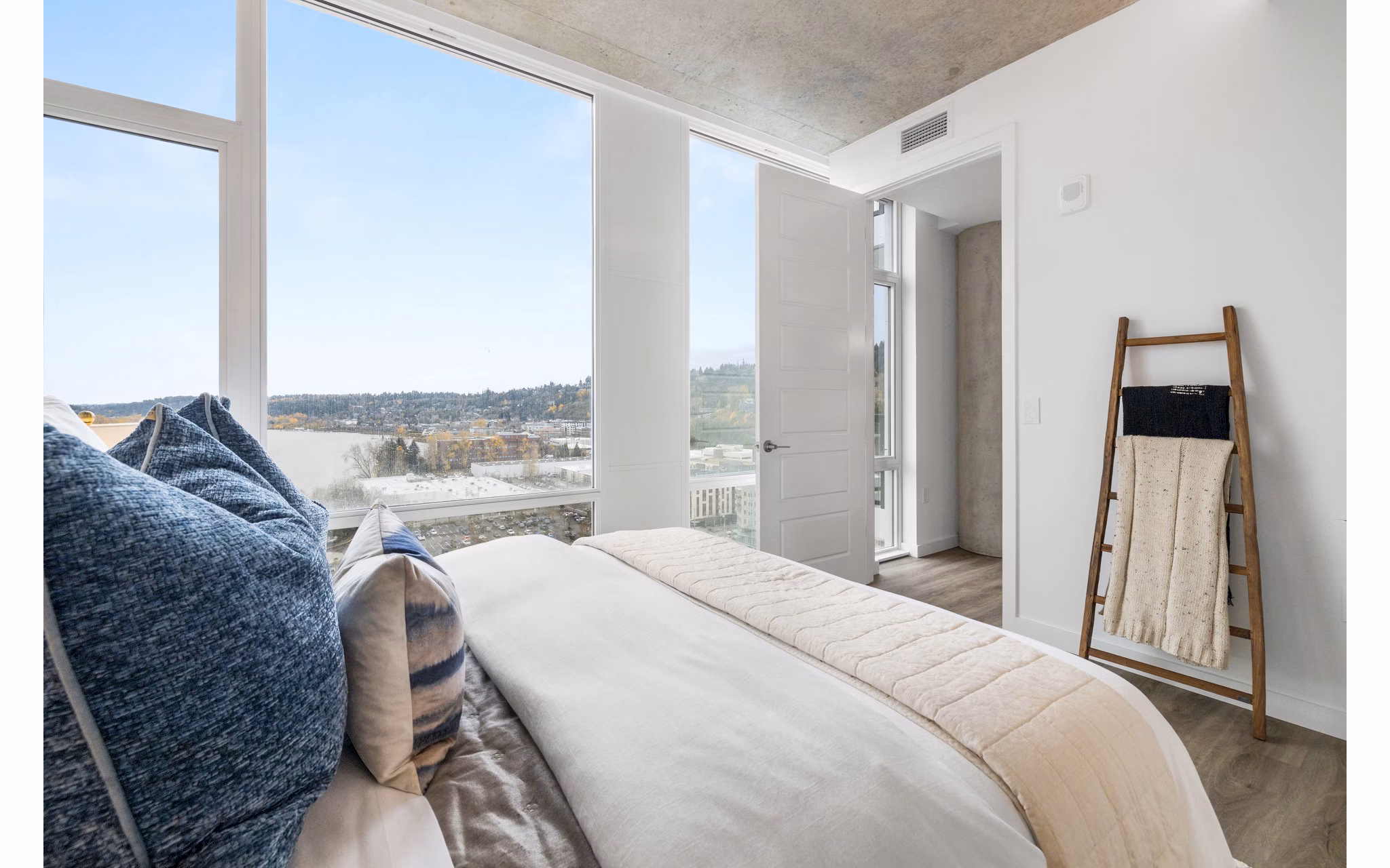 Luxurious bedroom with plush bedding and large windows at Willamette Tower Apartments in Portland, offering city views