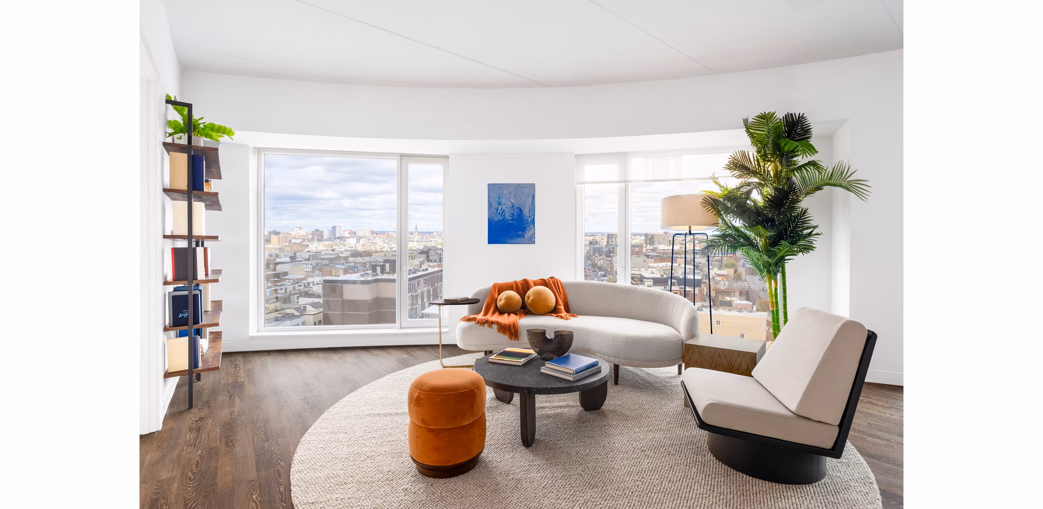 Living room with modern dÃ©cor and large windows at The Noble Apartments by Greystar