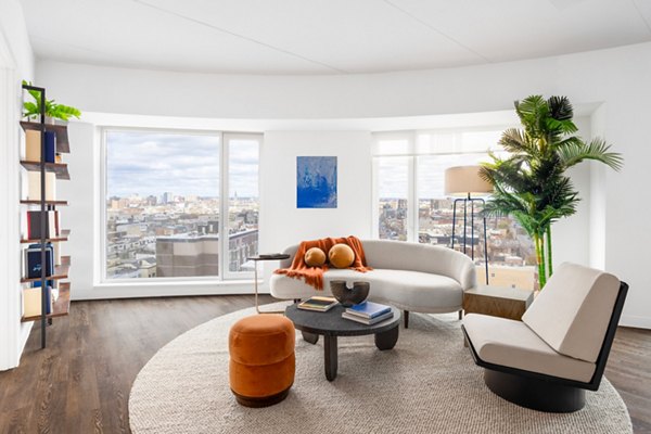 Living room with modern dÃ©cor and large windows at The Noble Apartments by Greystar