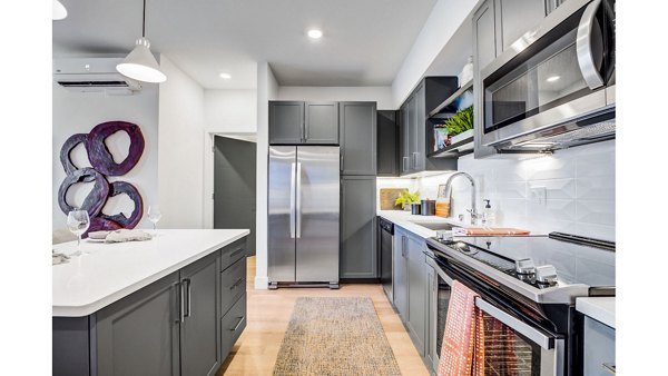 Modern kitchen featuring stainless steel appliances and marble countertops in The Eisley Apartments