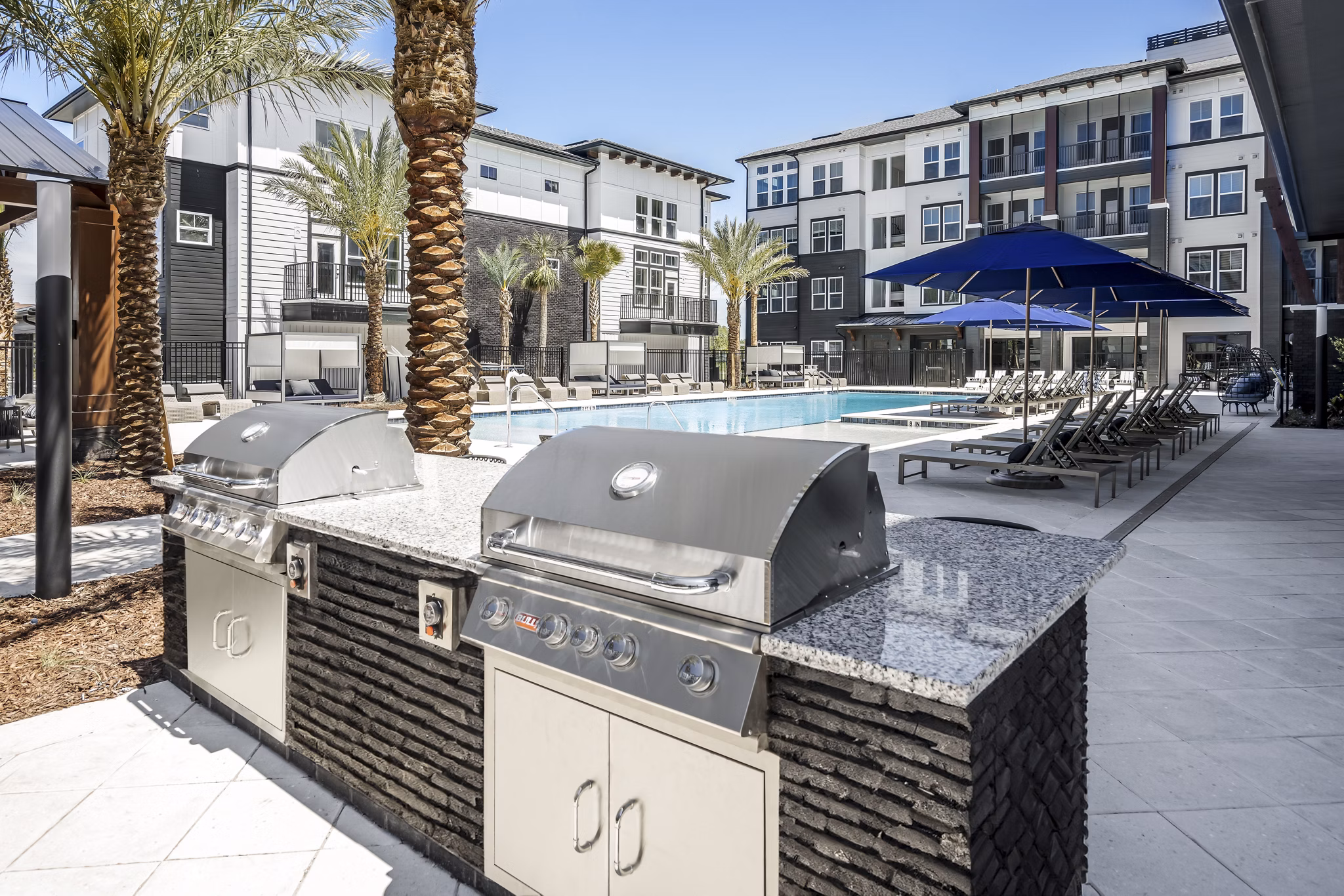Grill area and pool patio at The Elliott Apartments featuring modern outdoor seating and greenery