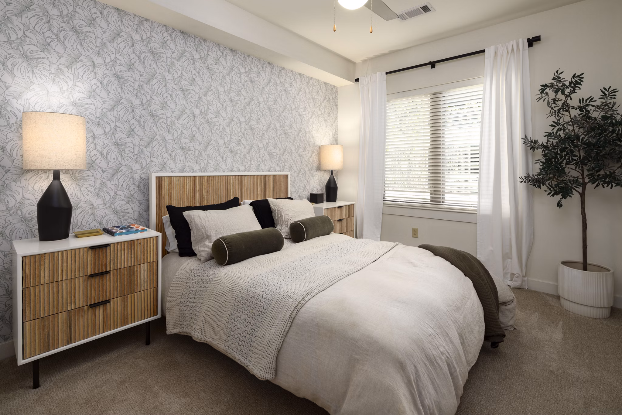 Spacious bedroom featuring a queen bed, stylish lamps, and a potted plant in luxury apartment