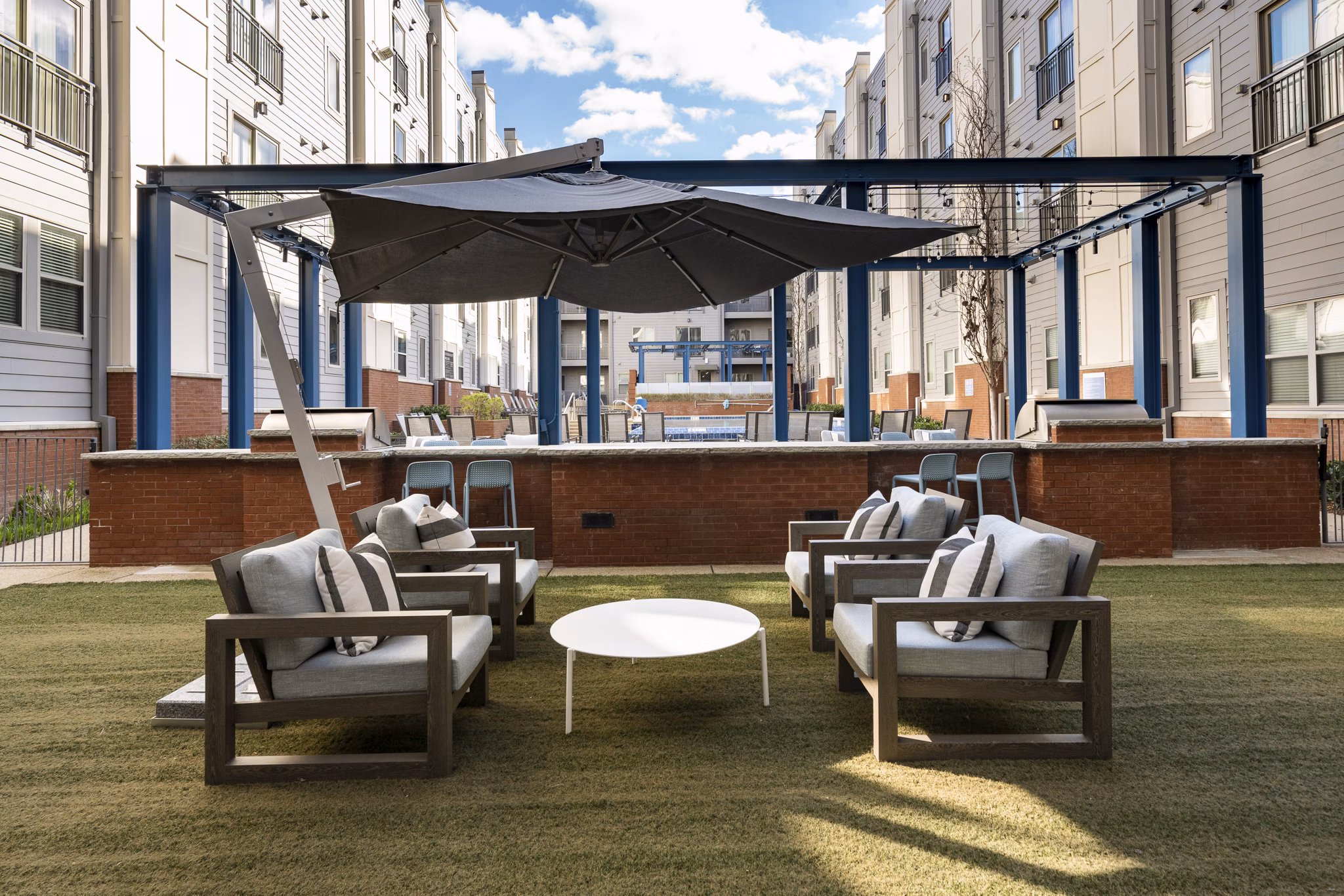 Outdoor seating area with chairs and a round table under a large umbrella in a courtyard of luxury apartments