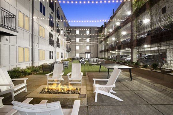 Outdoor patio with white chairs around a fire pit and string lights for cozy gatherings at luxury apartments