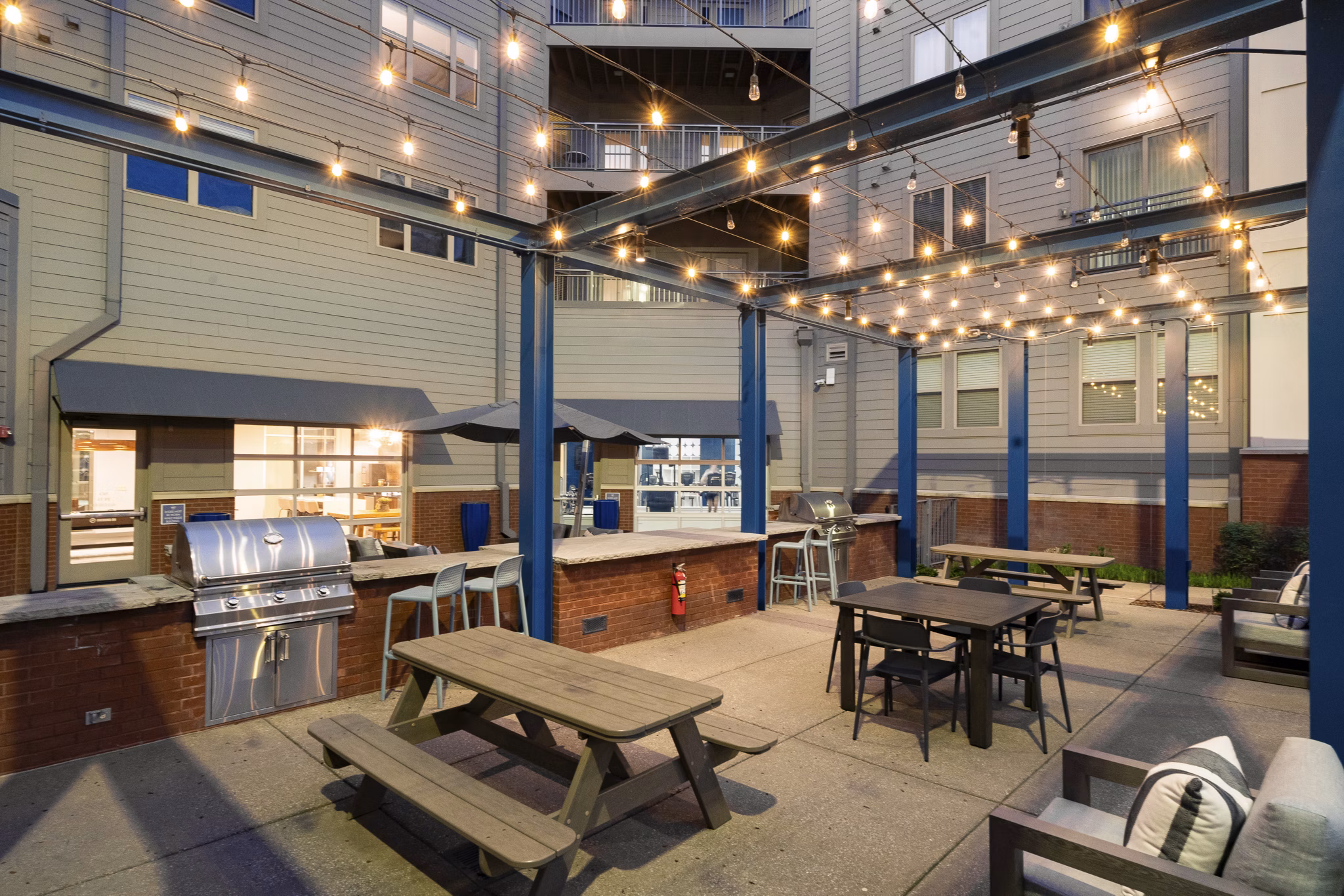Outdoor patio with picnic tables, string lights, and a grill at luxury apartments