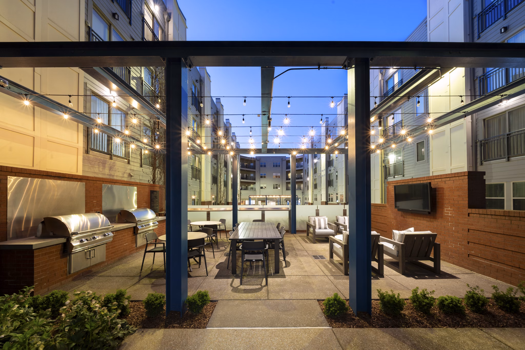 Outdoor patio area with string lights, tables, and grills at luxury apartments