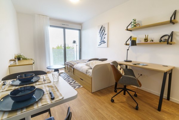 Bright bedroom with a desk, shelves, and large windows.