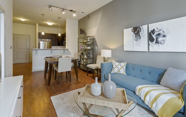 Modern living room and dining area with blue sofa, wooden table, and hardwood floors in luxury apartment