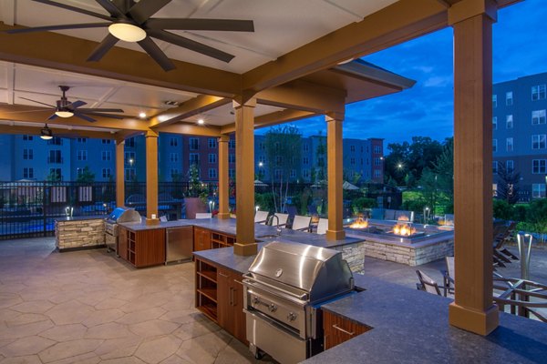 Outdoor grill area at Alta Clara at the Fells Apartments featuring modern seating and lush landscaping