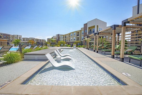 Luxurious pool area at Alta Denton Station Apartments featuring comfortable loungers and lush greenery