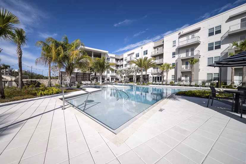 Pool with sundeck and palm trees at Novel Nona Apartments