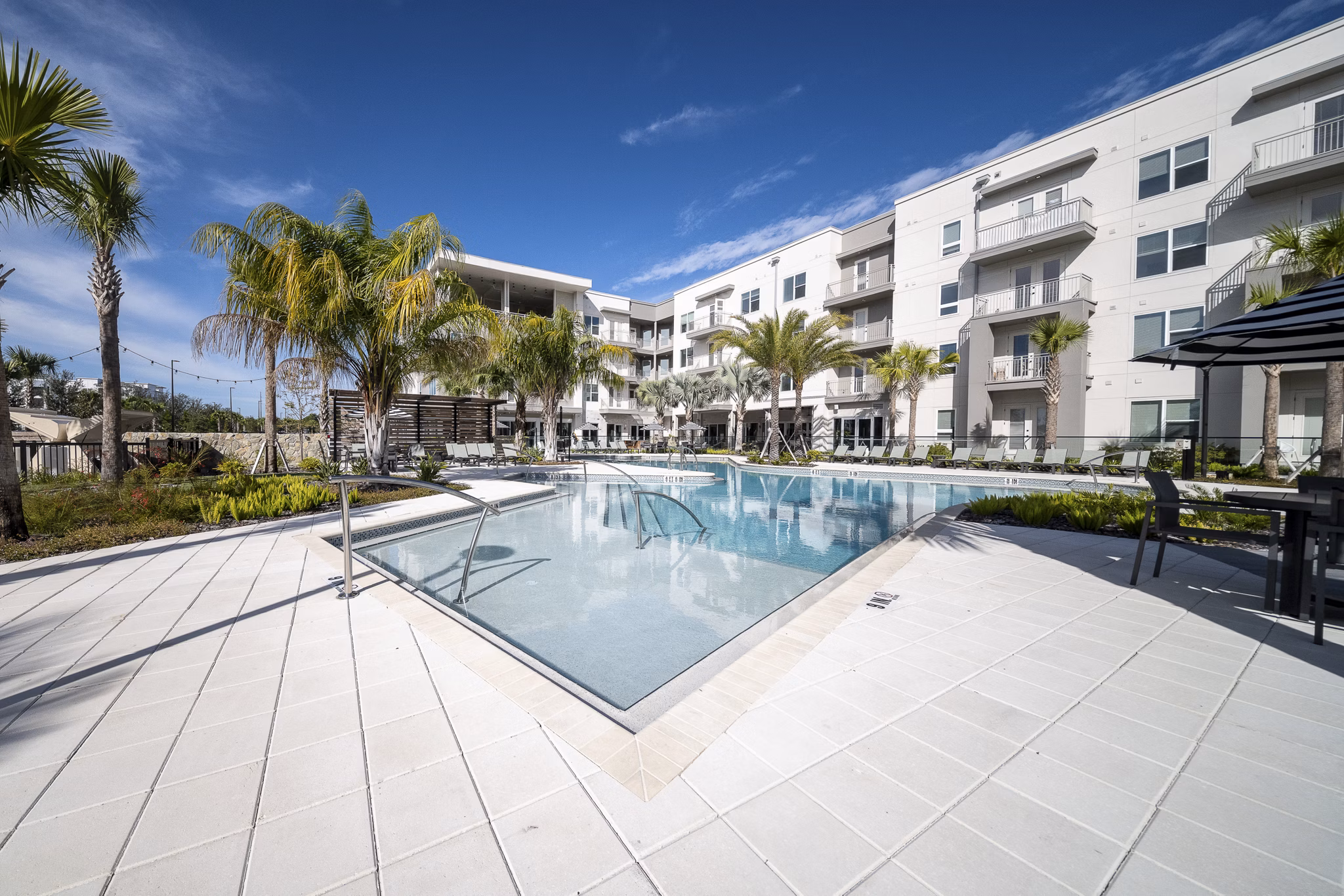 Pool with sundeck and palm trees at Novel Nona Apartments