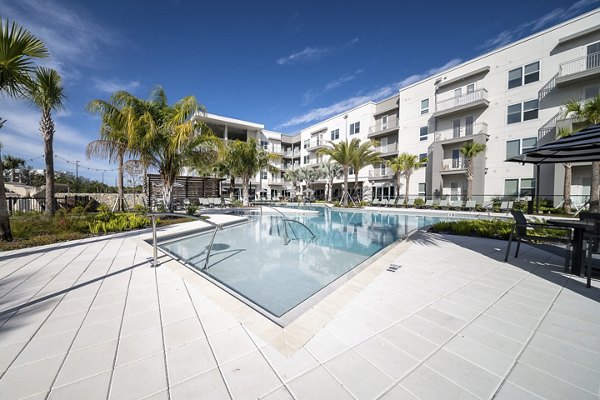Pool with sundeck and palm trees at Novel Nona Apartments