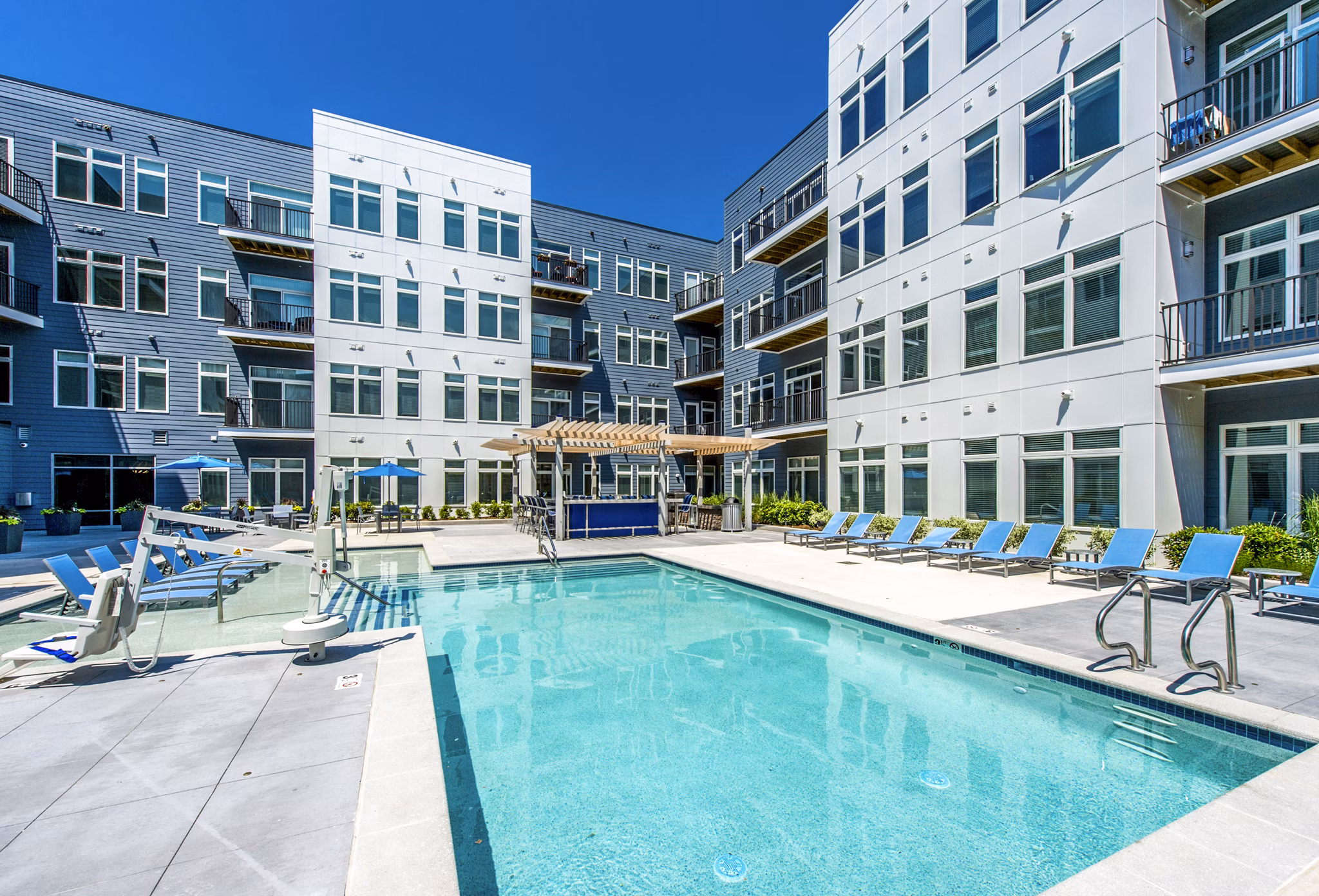 Inviting outdoor pool at Re150 Apartments with modern loungers and lush landscaping for relaxation and leisure
