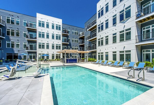 Inviting outdoor pool at Re150 Apartments with modern loungers and lush landscaping for relaxation and leisure