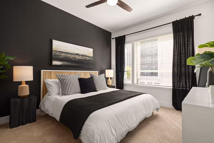 Modern bedroom featuring cozy furnishings and large windows at Tens on West Apartments luxury living