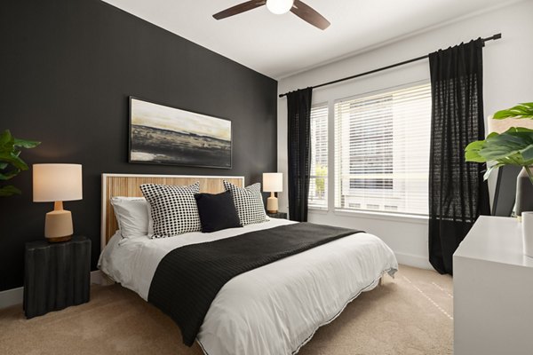 Modern bedroom featuring cozy furnishings and large windows at Tens on West Apartments luxury living