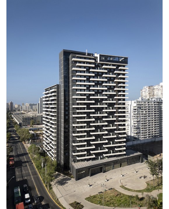 Modern high-rise building with balconies in a cityscape under a clear blue sky.