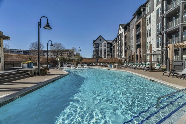 Luxurious pool at Alexan Research Park Apartments with poolside lounge chairs and lush landscaping, perfect for relaxation and leisure activities