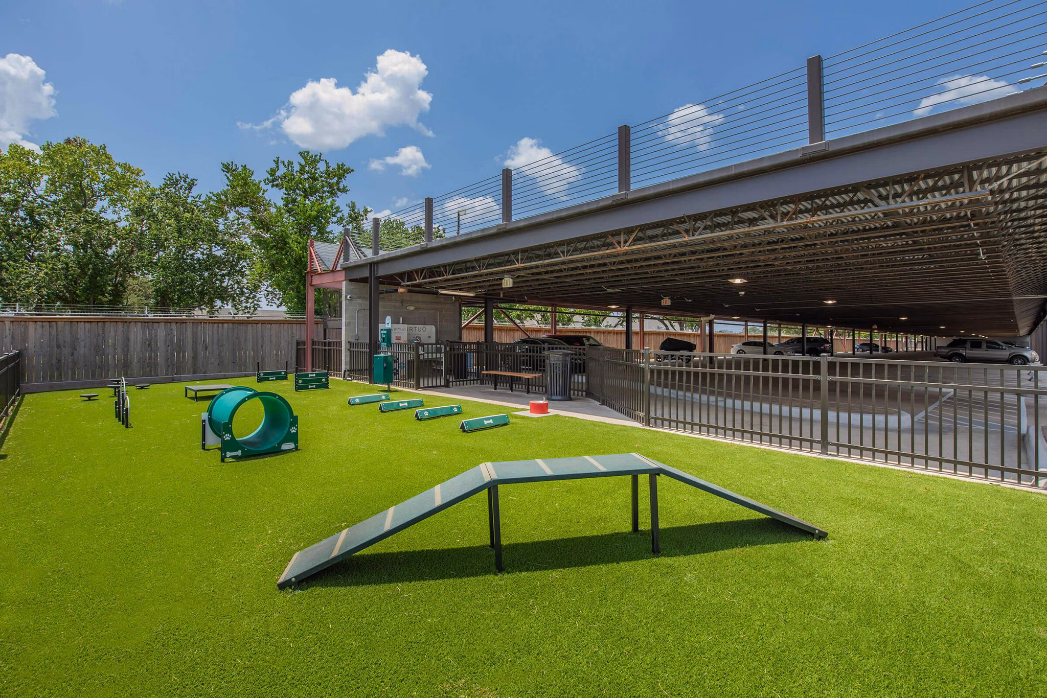 Spacious dog park at Vibe Med Center Apartments featuring shaded seating and agility equipment for residentsâ€™ pets