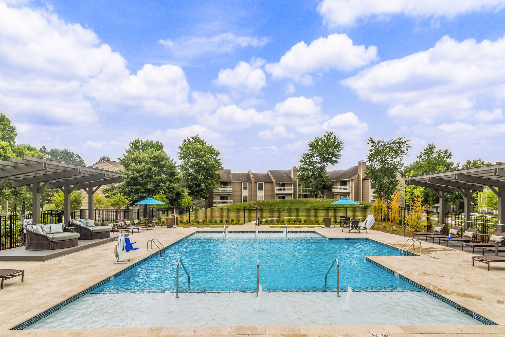 Relaxing poolside area featuring sun loungers and palm trees at Avana Matthews Apartments