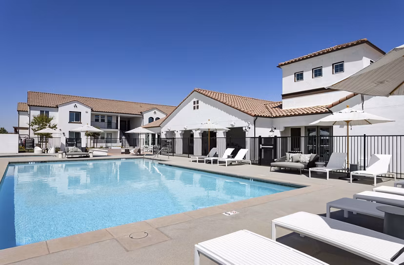 Sunny swimming pool area with lounge chairs and umbrellas in luxury Mediterranean-style apartments