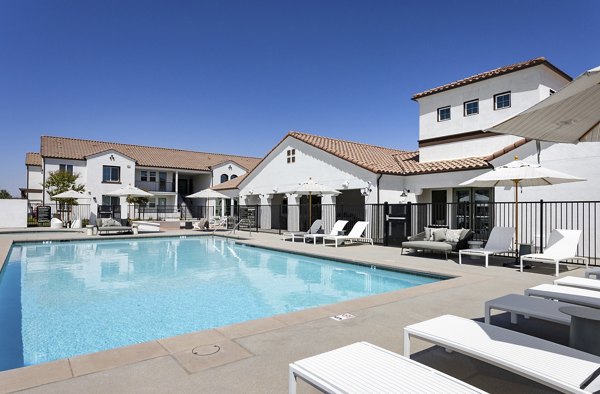 Sunny swimming pool area with lounge chairs and umbrellas in luxury Mediterranean-style apartments