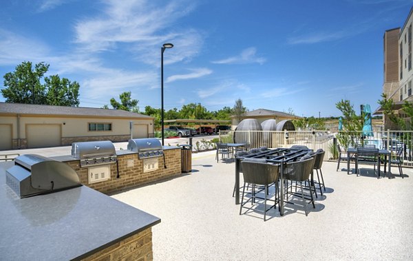 Outdoor grill area at Jovie Pflugerville Apartments featuring modern seating and BBQ pits