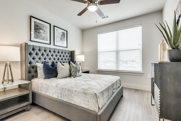 Modern bedroom featuring elegant decor and large windows at The District in Little Elm Apartments
