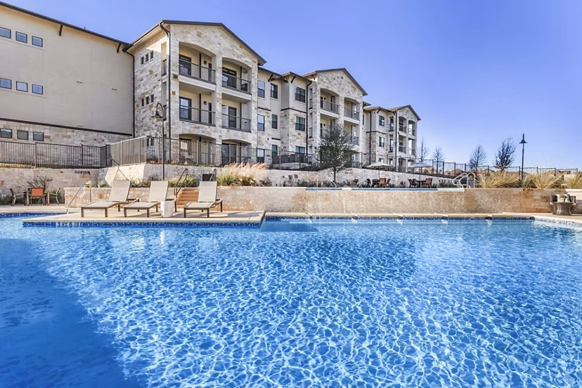 Luxury pool at Agora Stone Oak Apartments with surrounding sun loungers and landscaped greenery