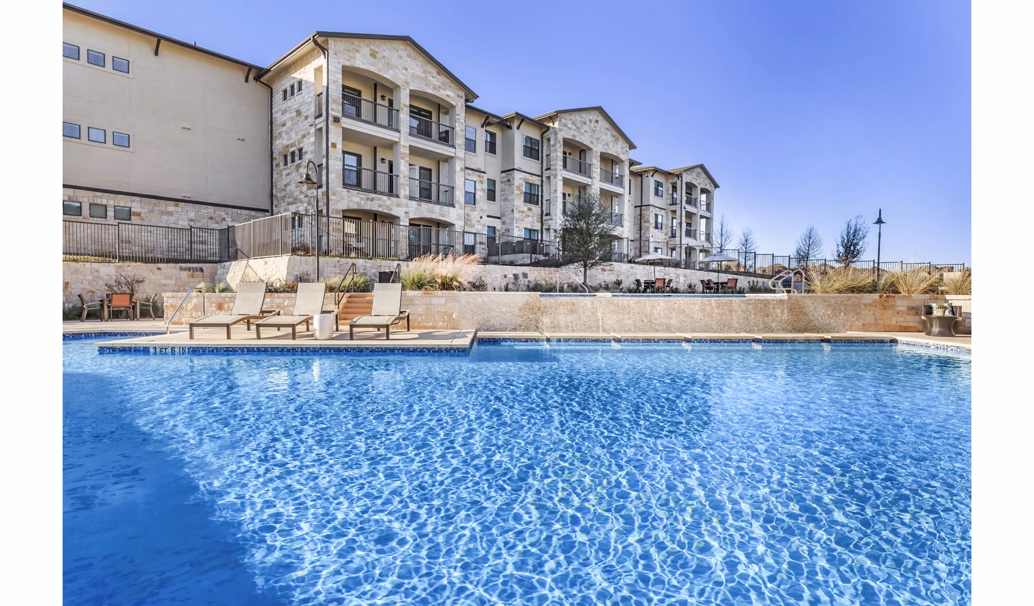 Luxury pool at Agora Stone Oak Apartments with surrounding sun loungers and landscaped greenery
