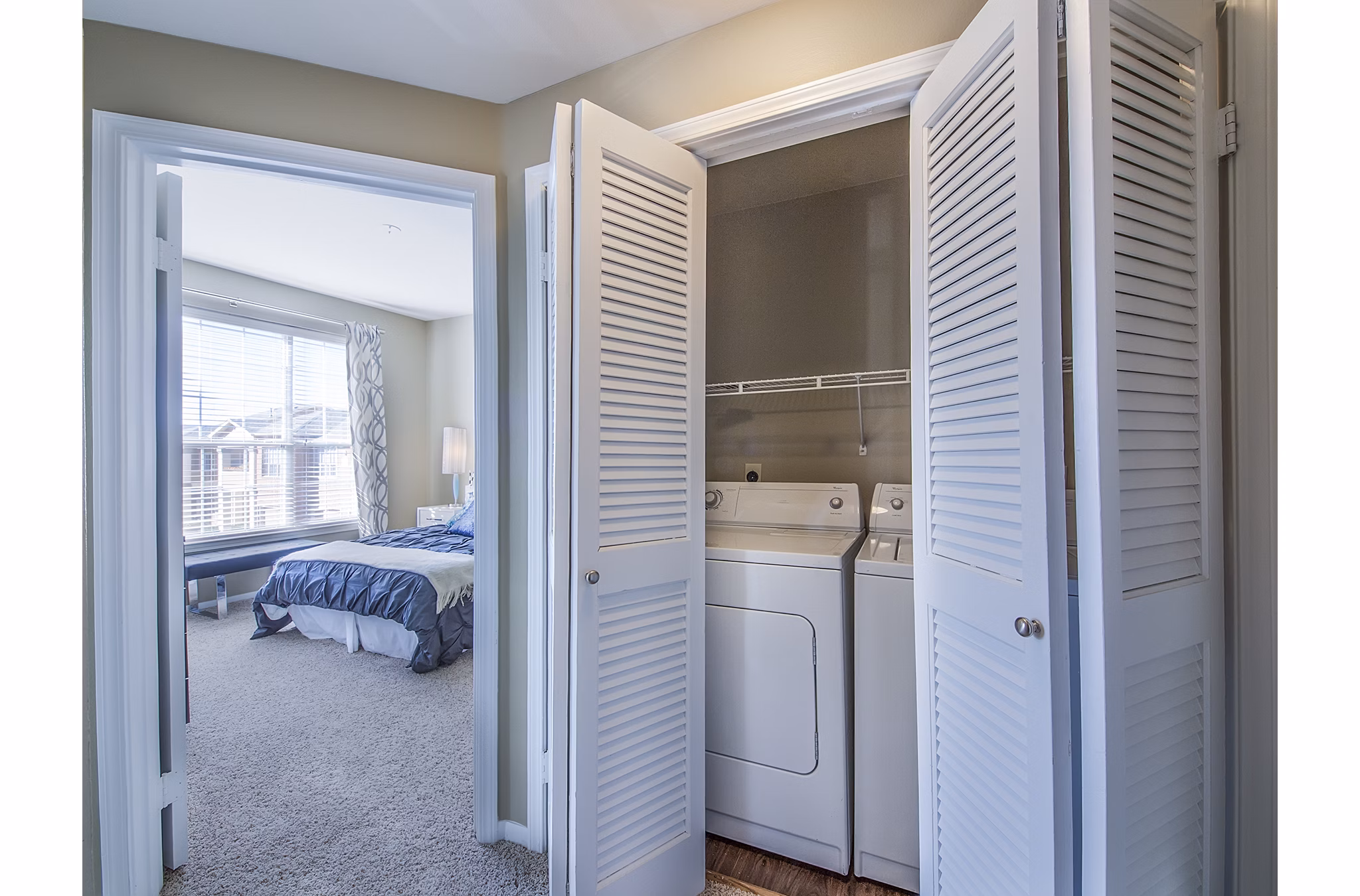 Laundry area with washer and dryer and a view into a spacious bedroom in luxury apartments