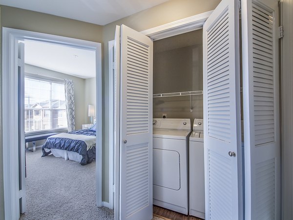 Laundry area with washer and dryer and a view into a spacious bedroom in luxury apartments