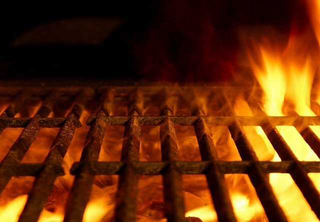 Intense flames beneath a dark grill grate, glowing in a warm, fiery light.