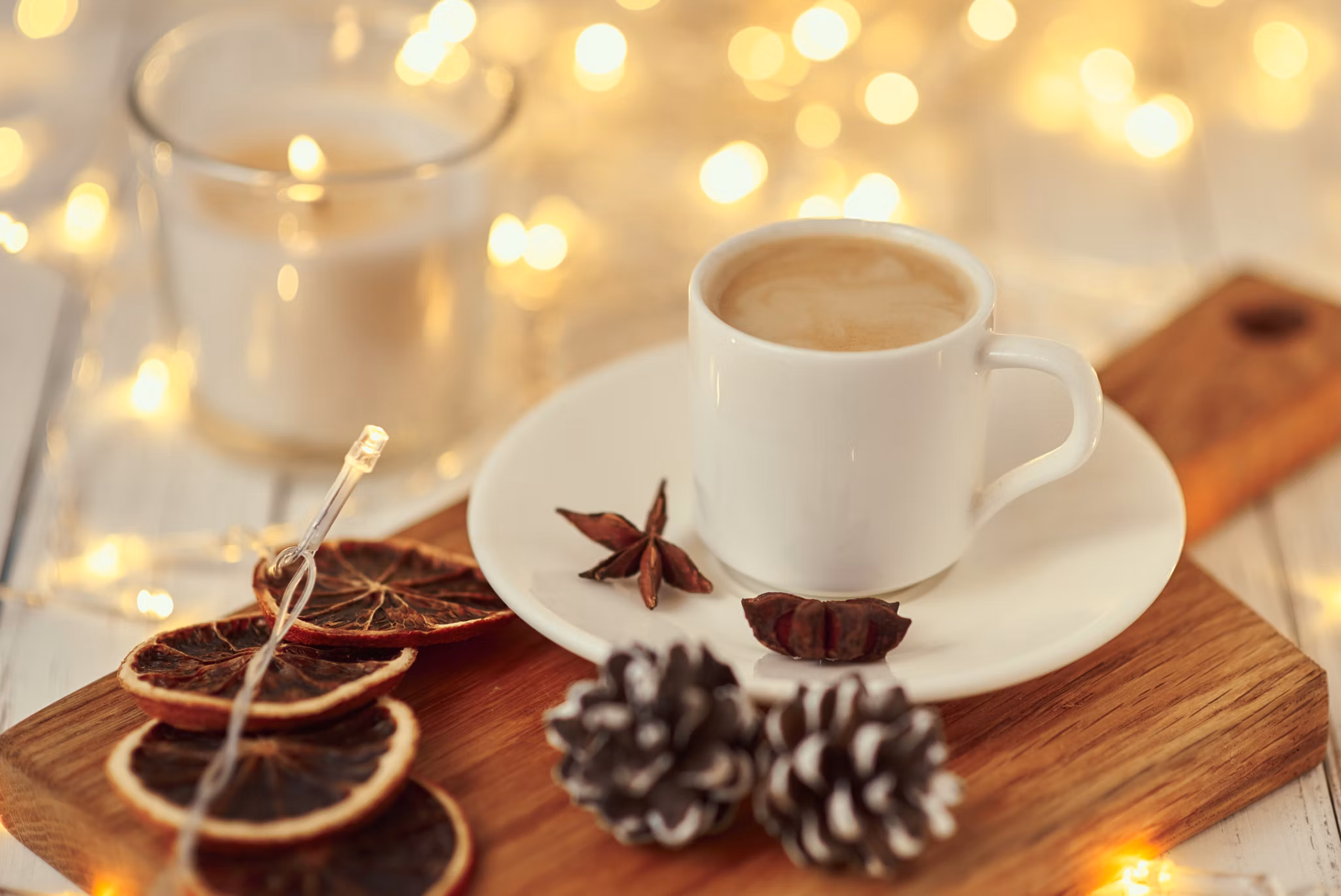 Cup of coffee with garland lights, burning candle and decoration on table. Cozy home concept