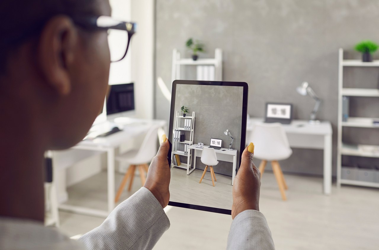 Black rental agent takes photo of apartment interior using smart tablet. Realtor video calling client, showing office workspace, giving tour around new home. Over shoulder device display close up view