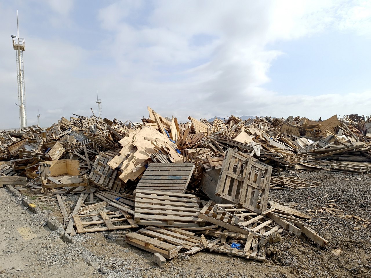 Wood waste collected for recycling outdoors in the Waste Center area. Mixed wood waste. Iron structure warehouse and mountains in the background of wood waste. Pile of Pallet Scrap Wood