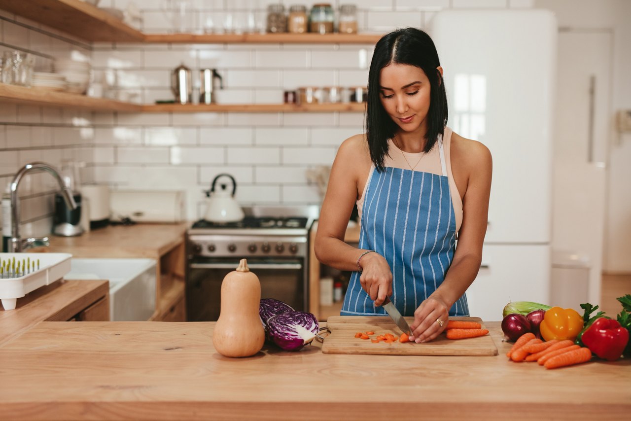Young woman preparing salad. Caucasian female cutting vegetables in kitchen at home.