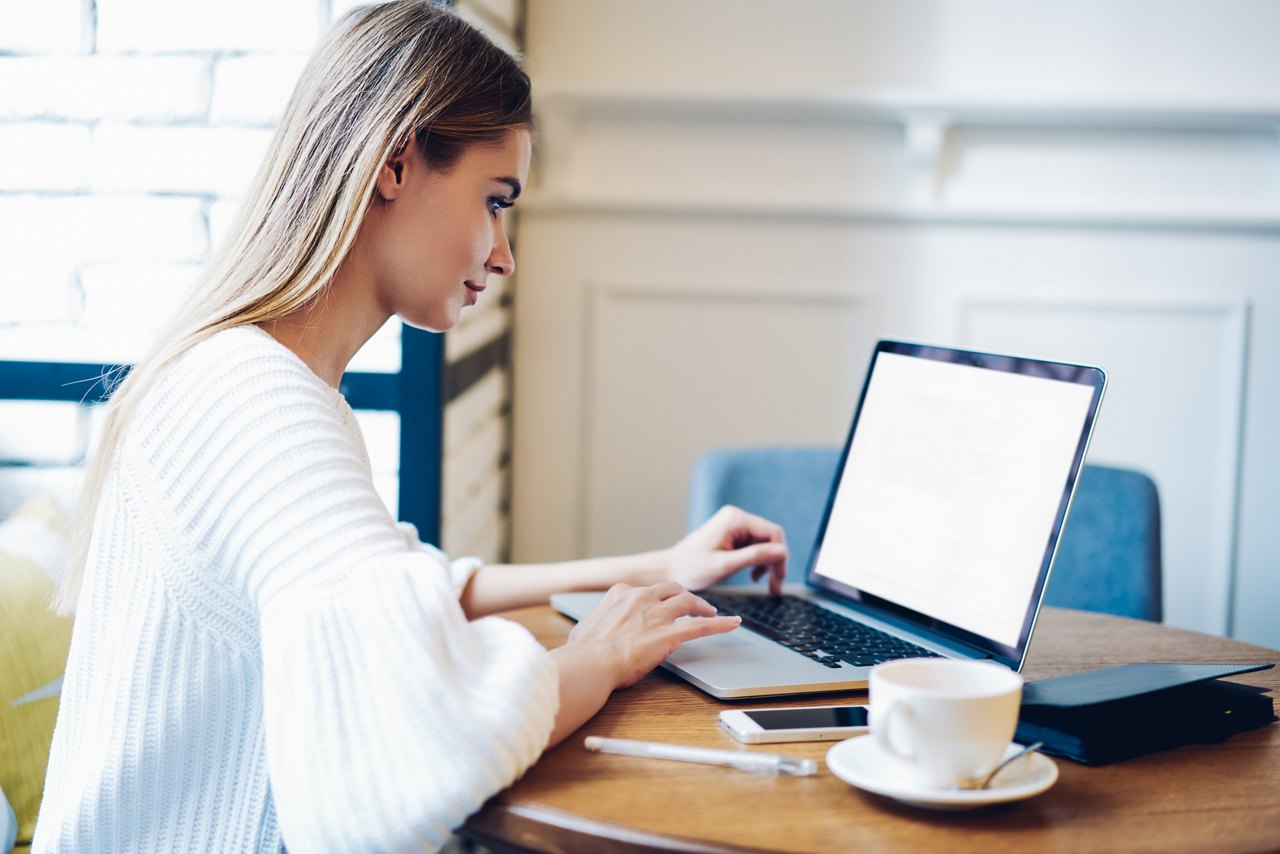Skilled female freelancer working remotely at modern laptop computer with blank screen area for IT advertising, side view of woman typing mock up text on copy space netbook using 4g wireless