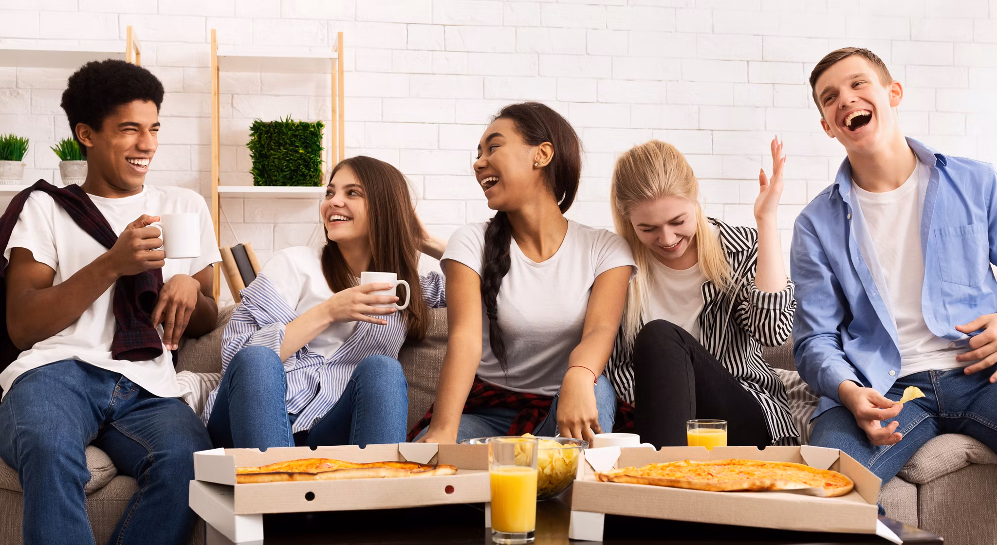 Happy teens eating pizza at home party, talking and laughing, panorama