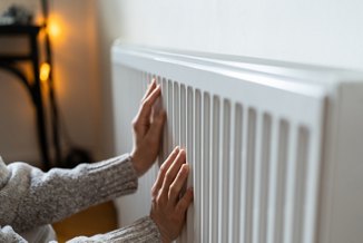 Closeup of woman in woolen sweater wants to keep warmth in apartment. Female puts hands on room central heating battery to warm up and prevent illness because of coldness. Person checks work of heater