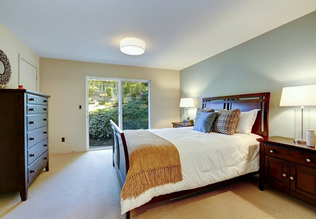 Bedroom with a large bed, wooden furniture, a ceiling light, and a sliding door opening to a garden.