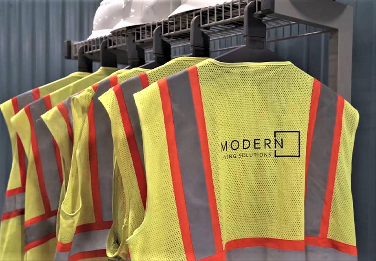 High-visibility safety vests with 'MODERN Living Solutions' branding hanging in a row with hard hats on top, indicating a focus on safety and professionalism.