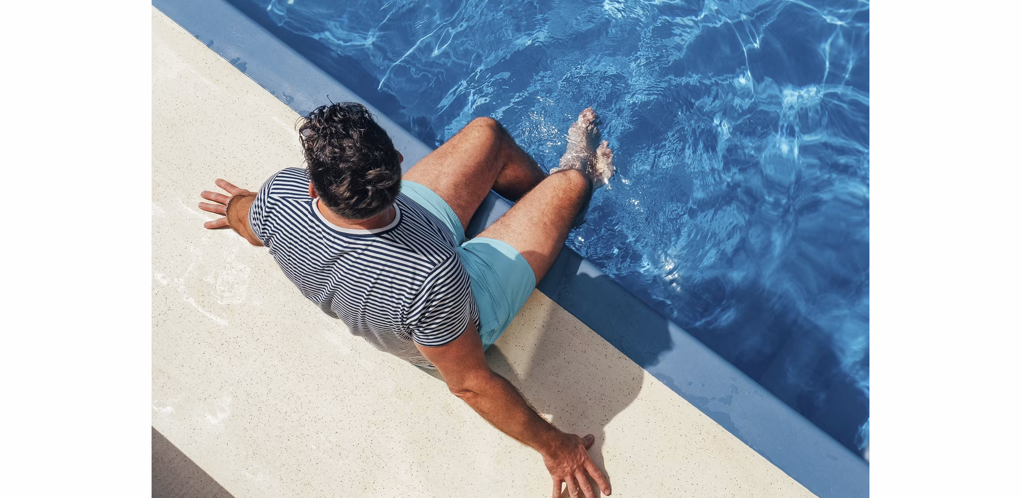 A man sitting at the edge of a pool with his feet in the water.